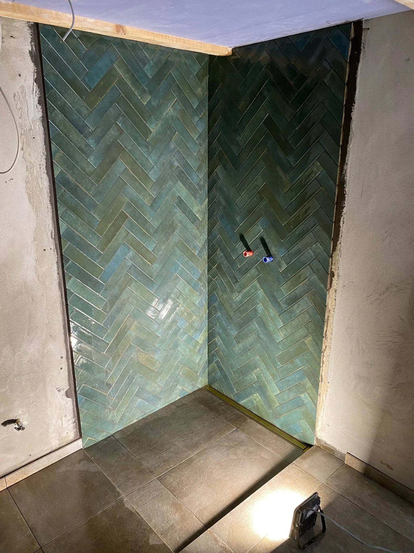 Indvendig væg med grønne, herringbone-fliser i badeværelse.