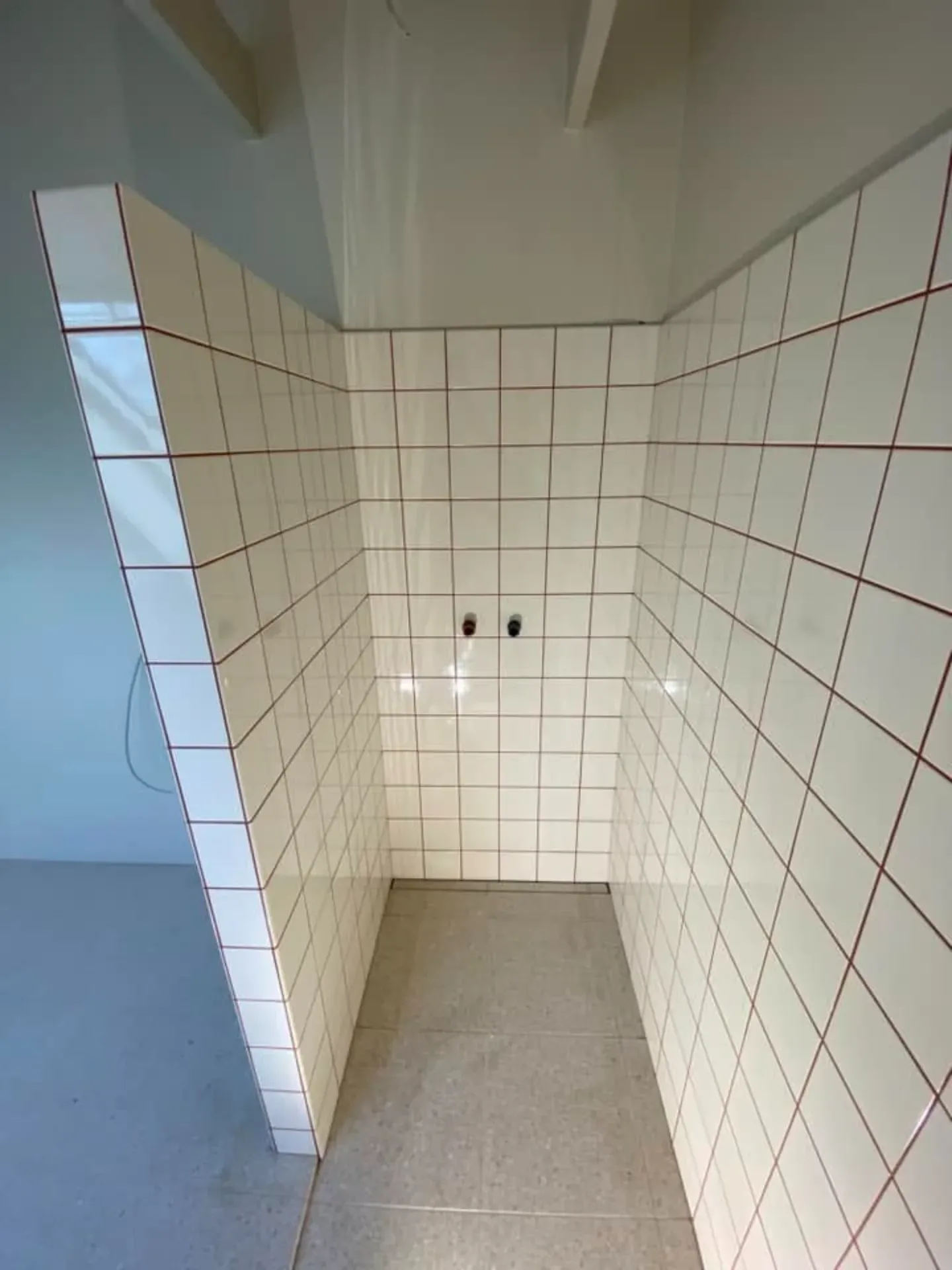 Badeværelsesvæg med hvide fliser og røde fuger.