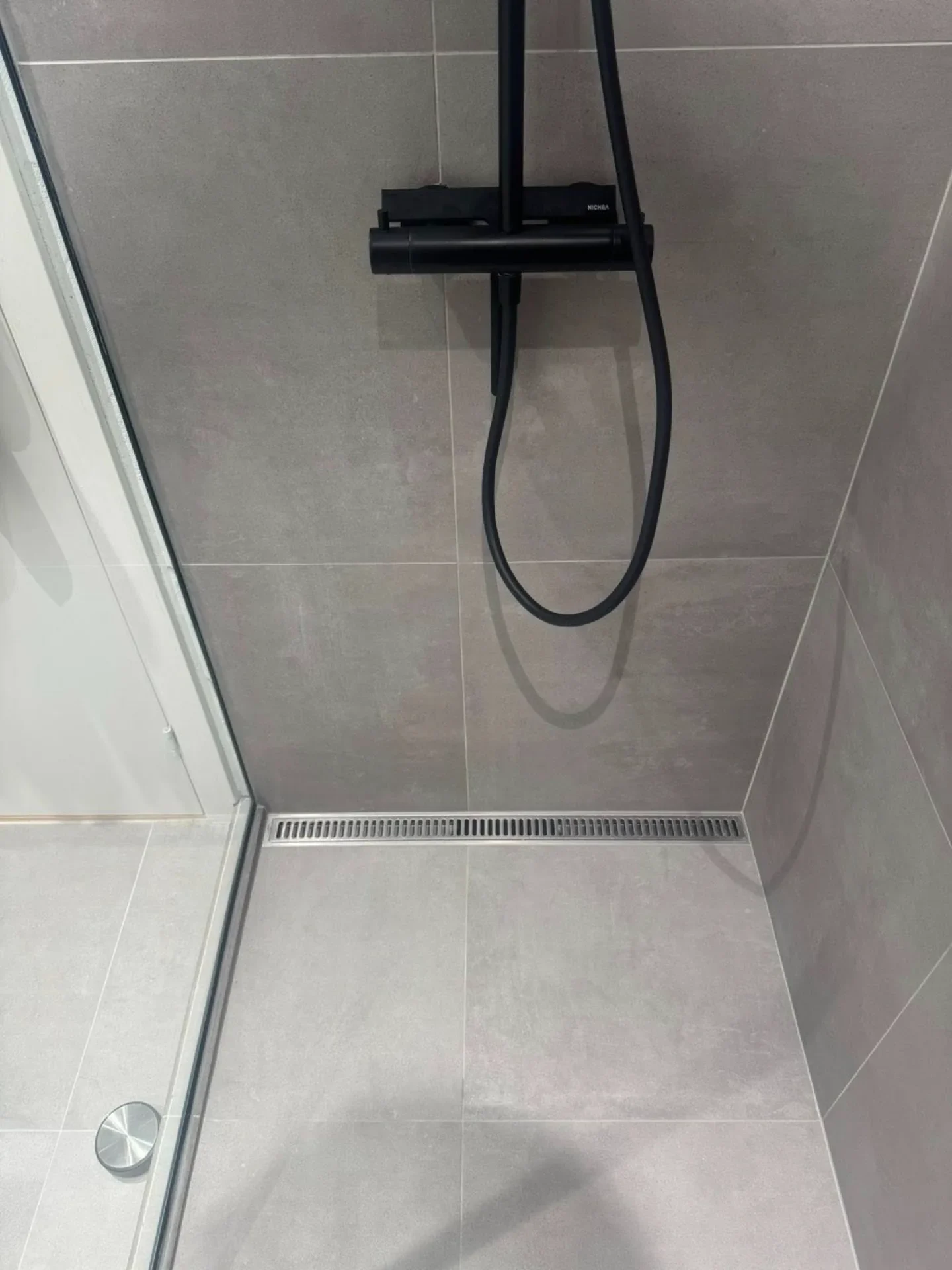 Sort bruserarmatur i moderne badeværelse med store grå fliser.